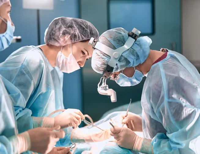 Two surgeons operating, one wearing microscope eyeware
